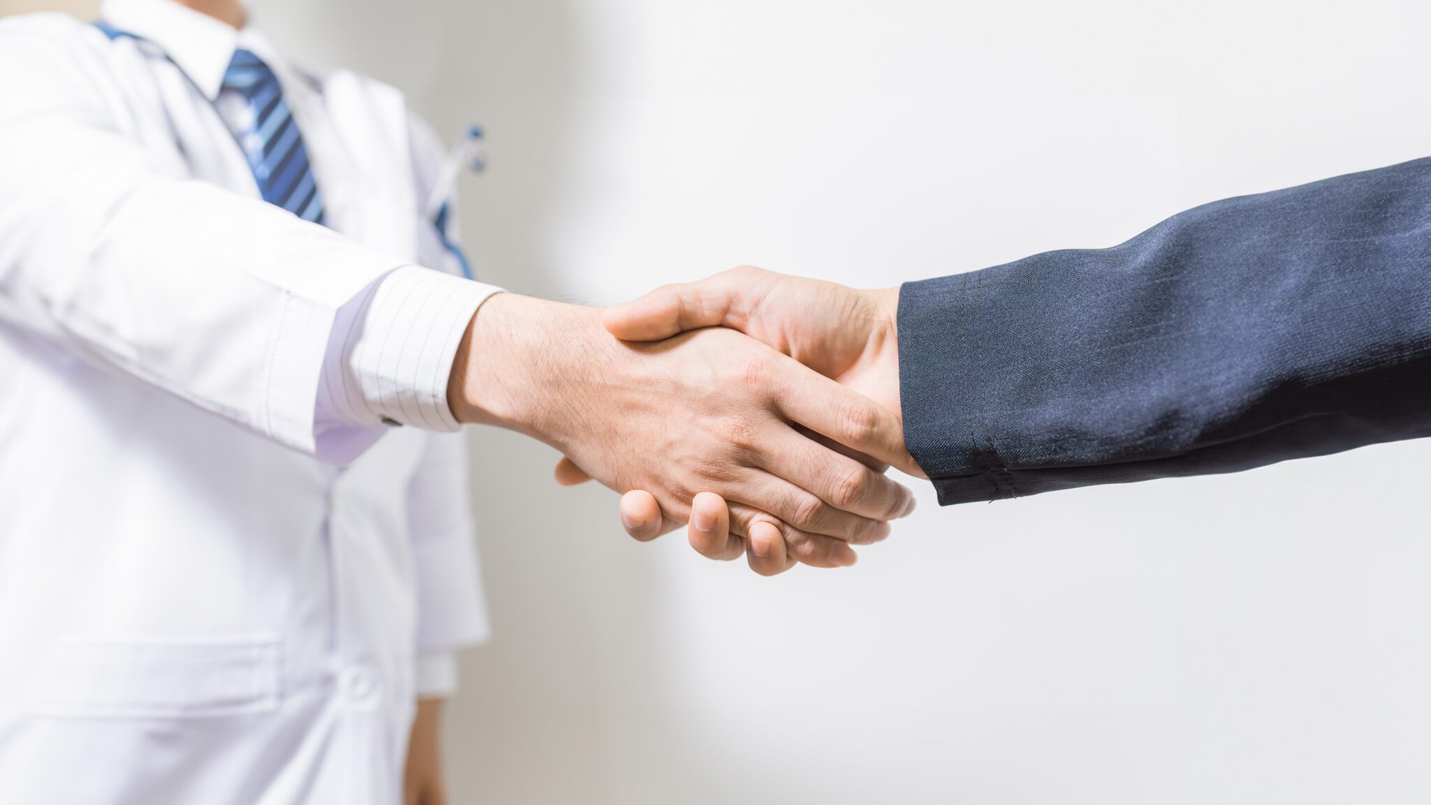 Two people shaking hands in front of a wall.