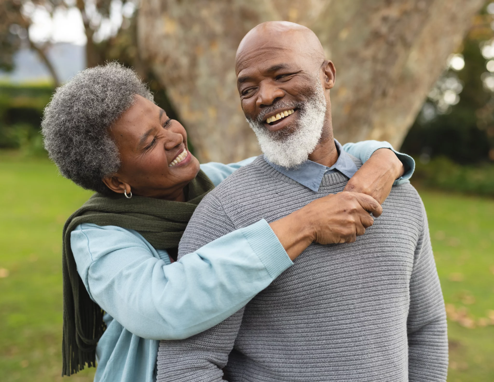 A woman hugging an older man in front of a tree.