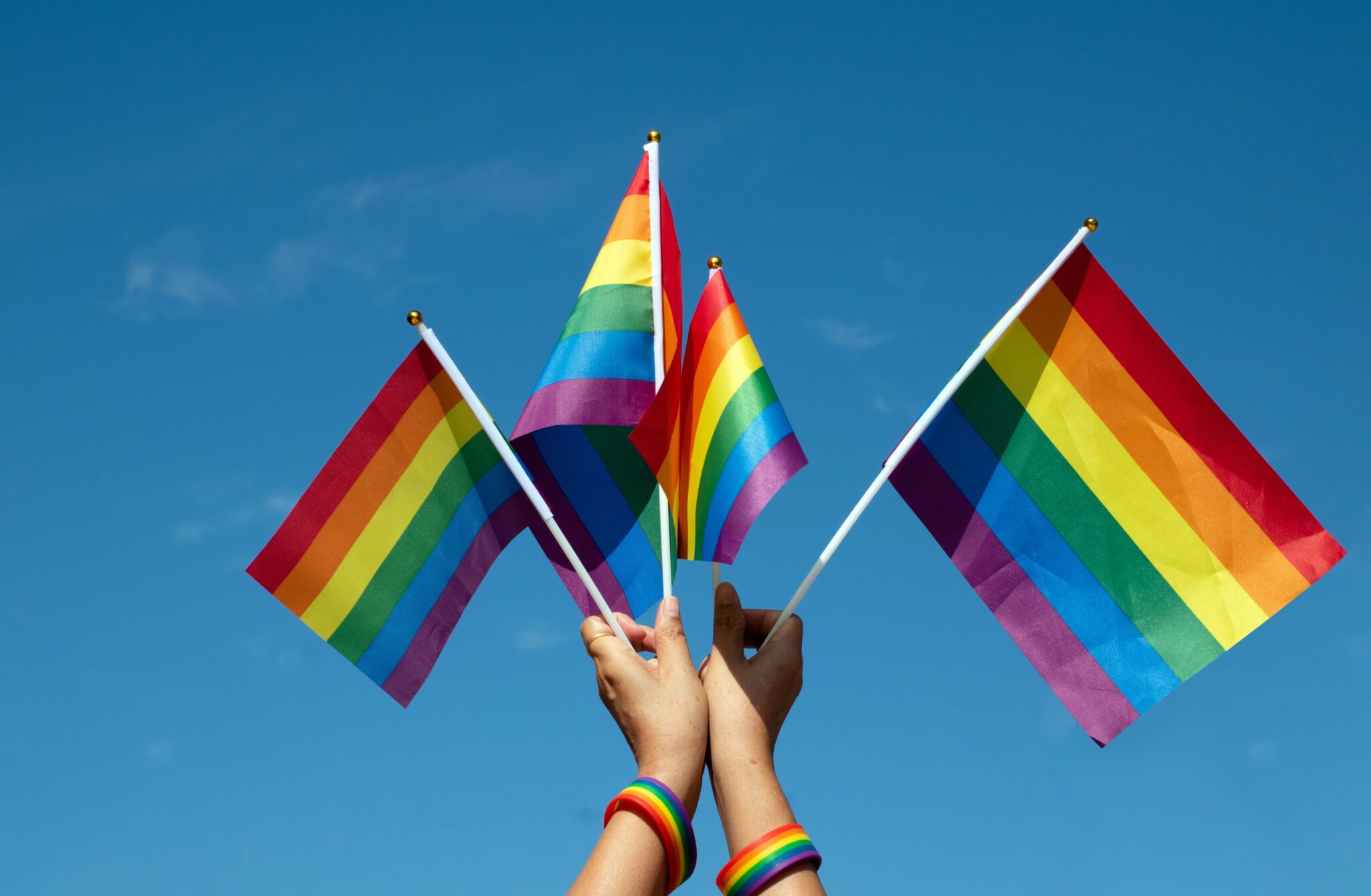 Three people holding rainbow flags in the air.