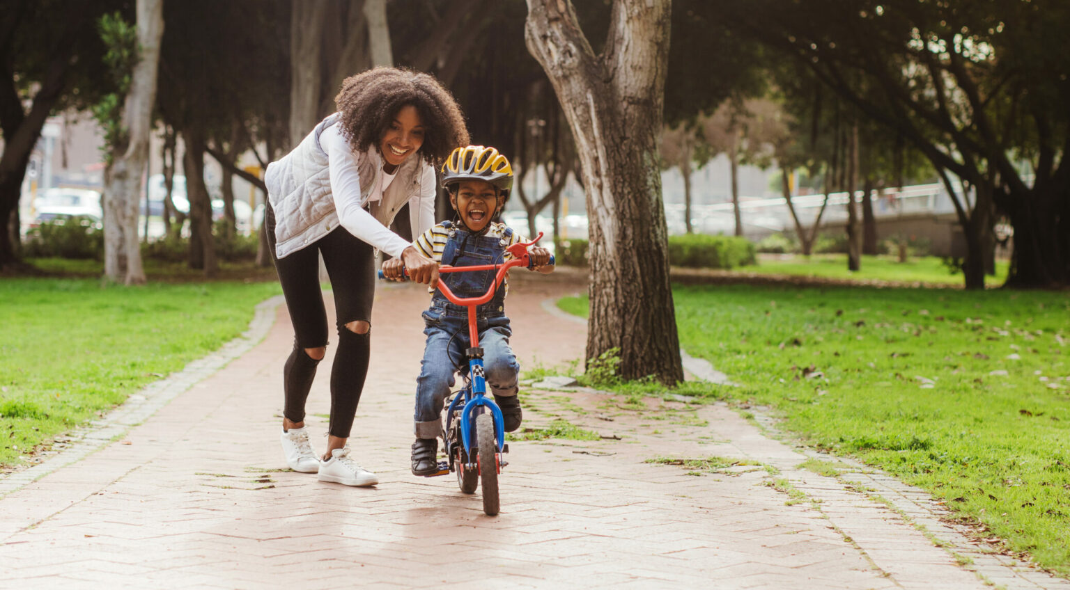 A woman helping a child ride a bike.