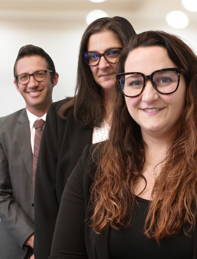 Three people in business attire and glasses smiling for the camera.