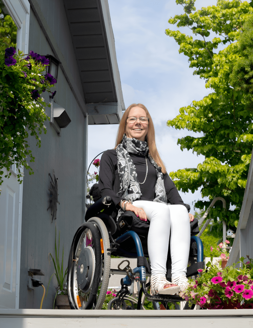 A woman in a wheelchair sitting on the side of a house.